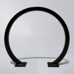 Black square-tube bike rack with a circular layout and square mounting bases, featuring a minimalist design suitable for securing bicycles.