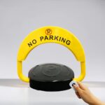 Front view of yellow D-type parking lock in raised position, shown with handheld remote control, equipped with reinforced motor and dry batteries for remote space control.