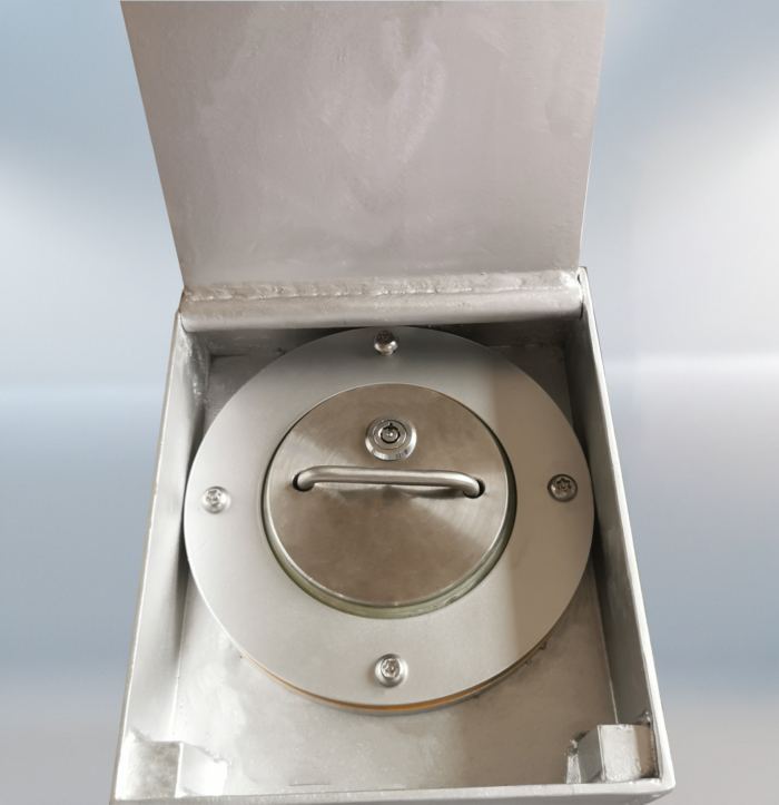 Close-up of manual stainless steel retractable bollard with handle, locking screws, and keyhole, in fully retracted position inside open base.