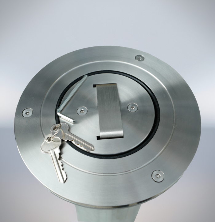 Close-up of the top of a stainless steel telescopic bollard, with keys and a metal tool, showing the unlocking mechanism details.
