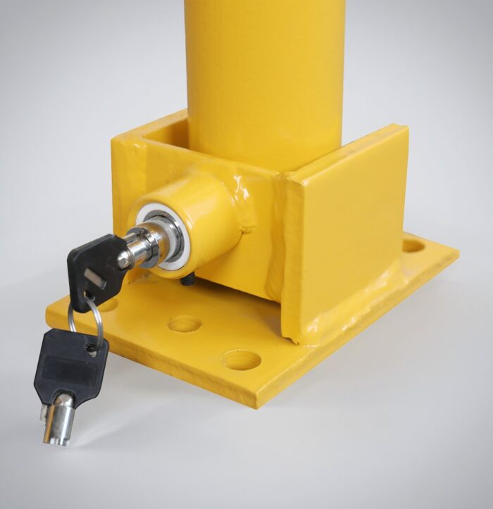 Close-up of yellow fold-down bollard with key-locking mechanism and spring-loaded structure for impact resistance, designed for parking lot safety and vehicle access control.