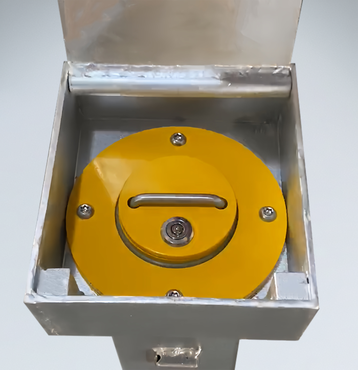 Close-up of manual carbon steel retractable bollard featuring handle, locking screws, and keyhole in retracted position within the open base.