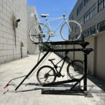 Outdoor view of KAVASS dual-assisted bike rack holding two bicycles, suitable for use in factory or industrial areas.