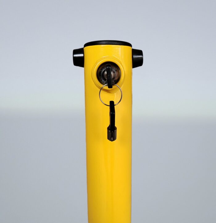 Close-up of built-in lock on yellow fold down bollard, highlighting secure key-inserted locking mechanism for controlled vehicle access.
