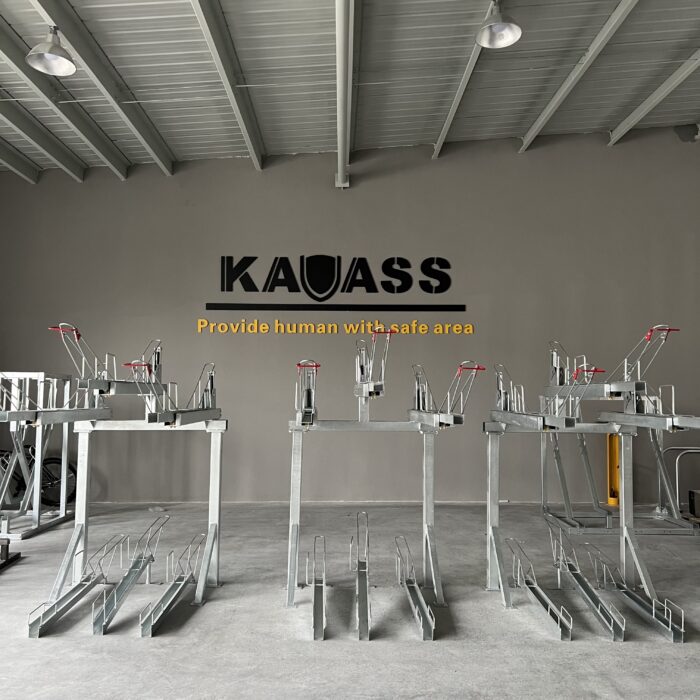 Gas Assist Double Decker Bike Rack, multiple sets arranged indoors without bicycles, featuring the 'KAVASS' logo and the slogan 'Provide human with safe area' on the wall.